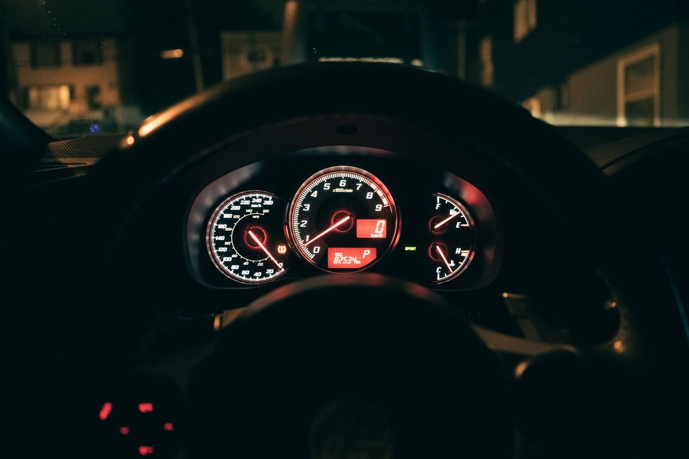 An illuminated car instrument cluster seen through the steering wheel at night