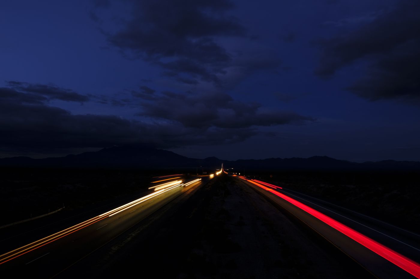 Long-exposure photo of headlight and taillight streaks on a divided highway at dusk under a dark cloudy sky