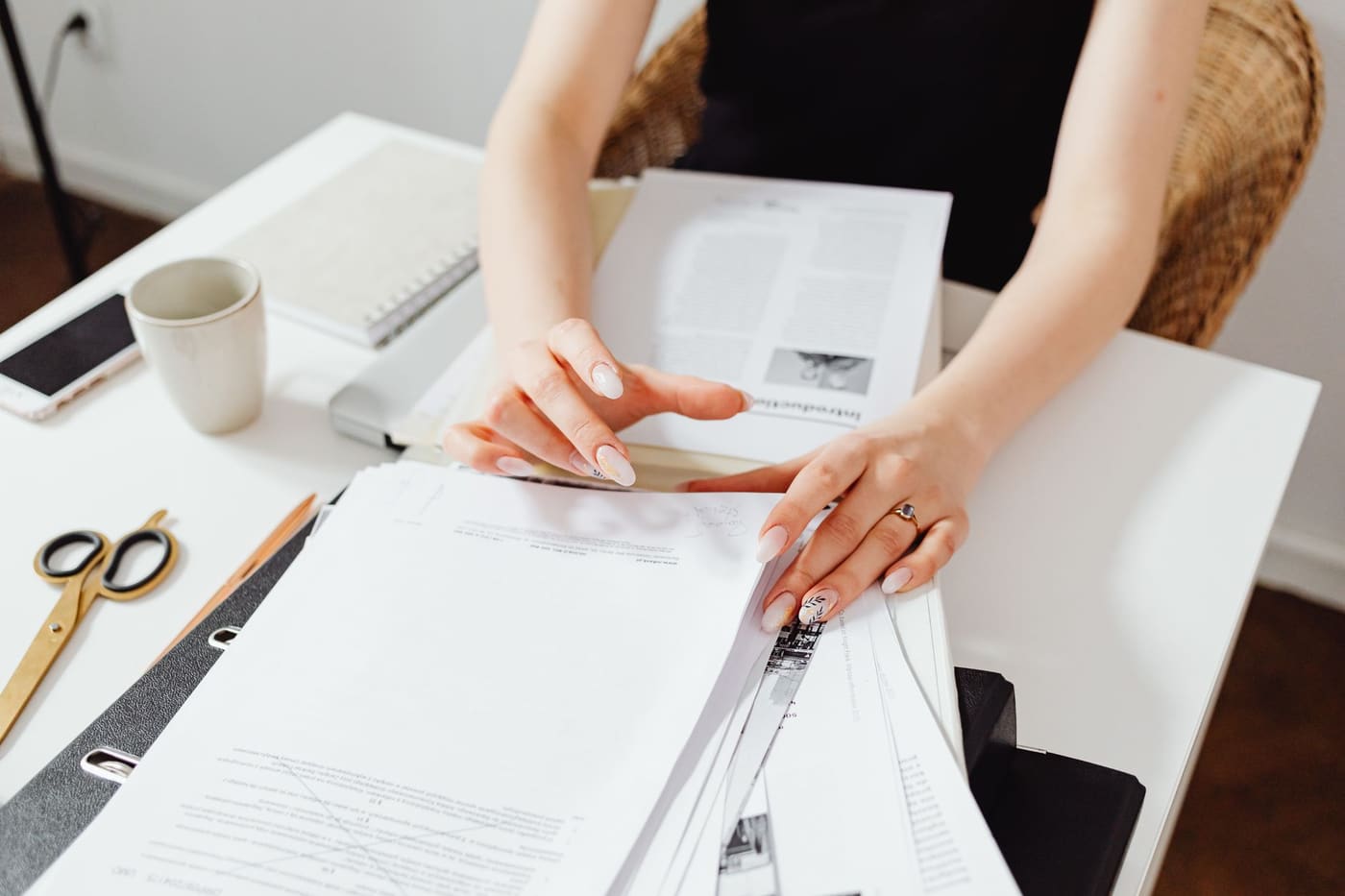 Hands sorting a stack of papers and folders on a desk at home
