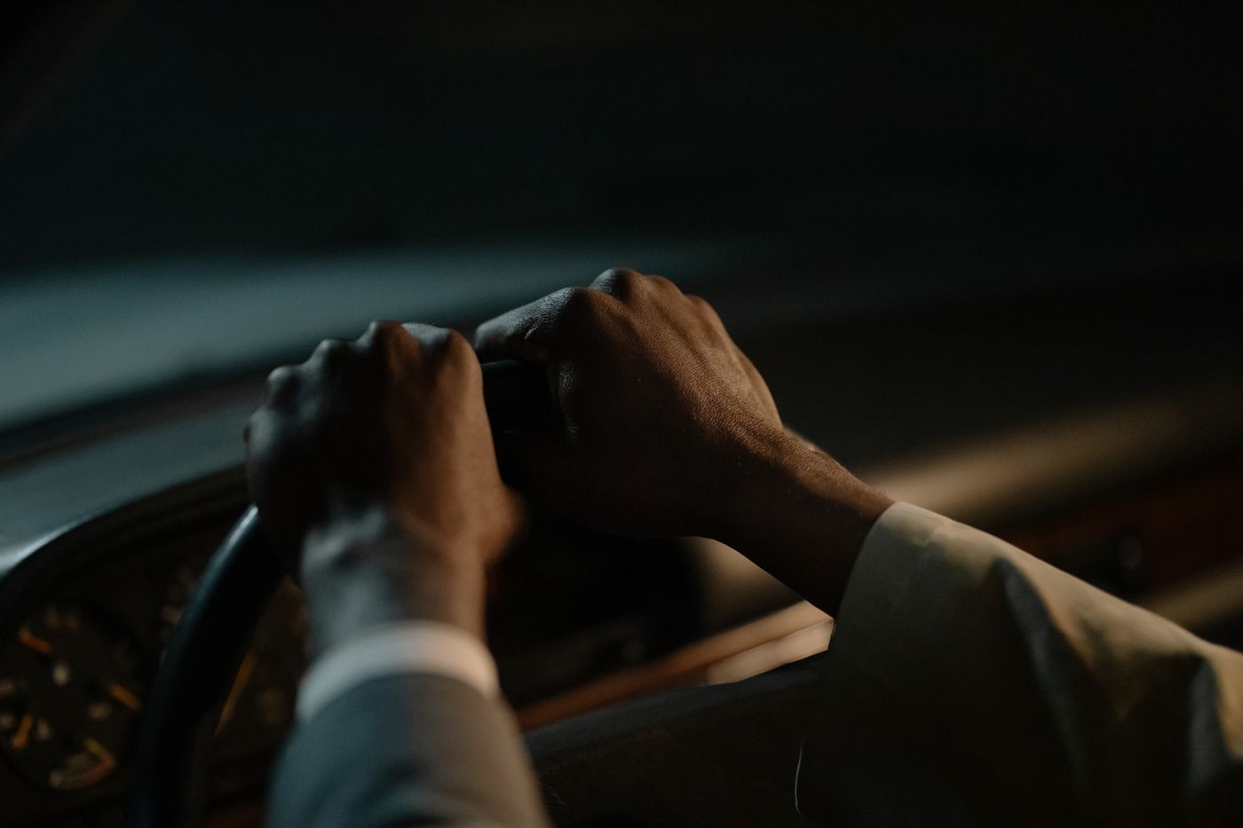 A driver's hands resting on a steering wheel inside a dark car at night