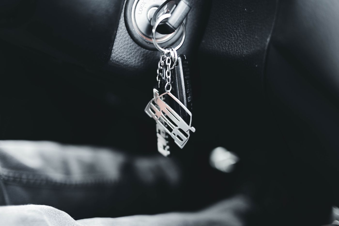 A car key with a metal car-shaped keychain hanging from an ignition switch