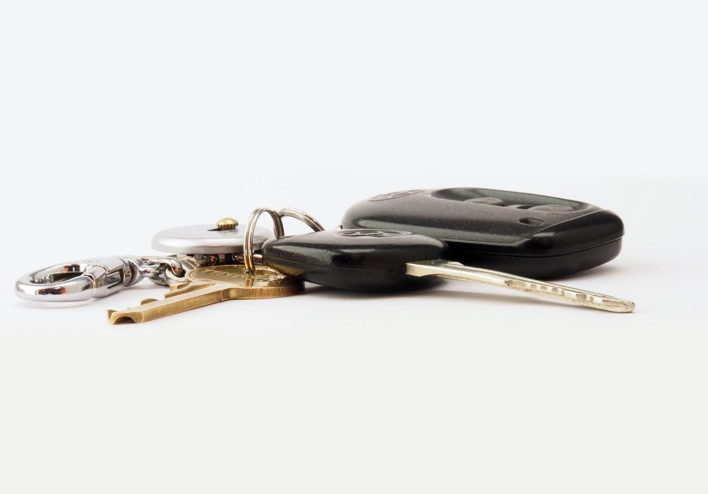 A set of car keys with a black remote fob and two metal keys resting on a white surface