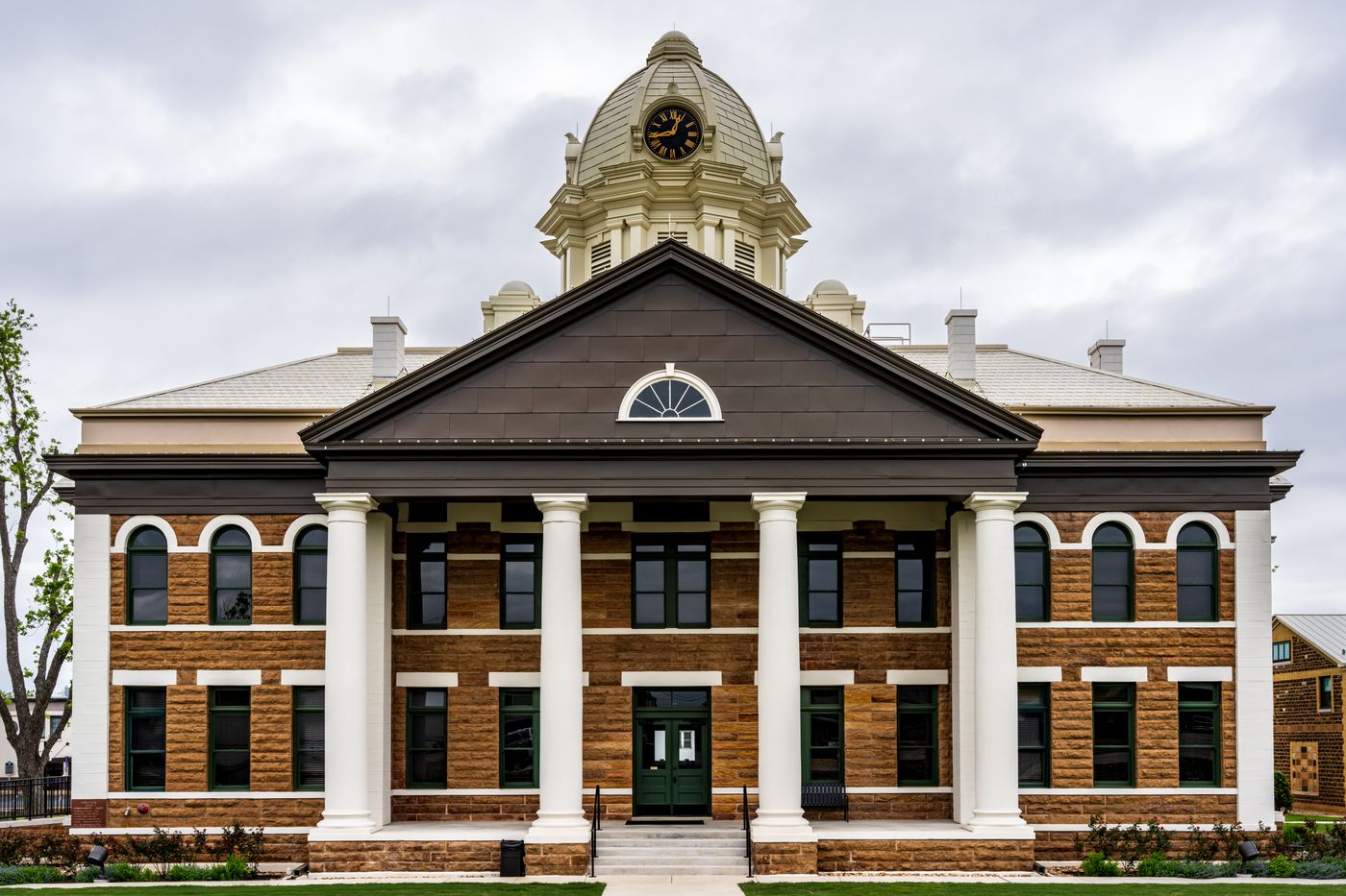 A historic brick and stone county courthouse with white columns and a clock tower under a cloudy sky