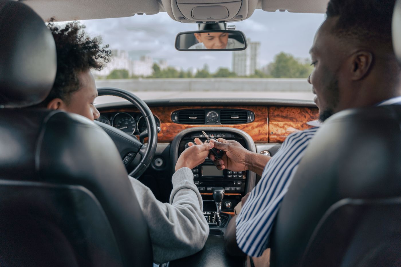 A teenager in the driver's seat taking car keys from an adult in the passenger seat